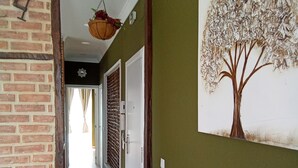 Une pièce avec un mur en briques, un mur vert orné d’un tableau représentant un arbre, un canapé avec un coussin et un panier suspendu.