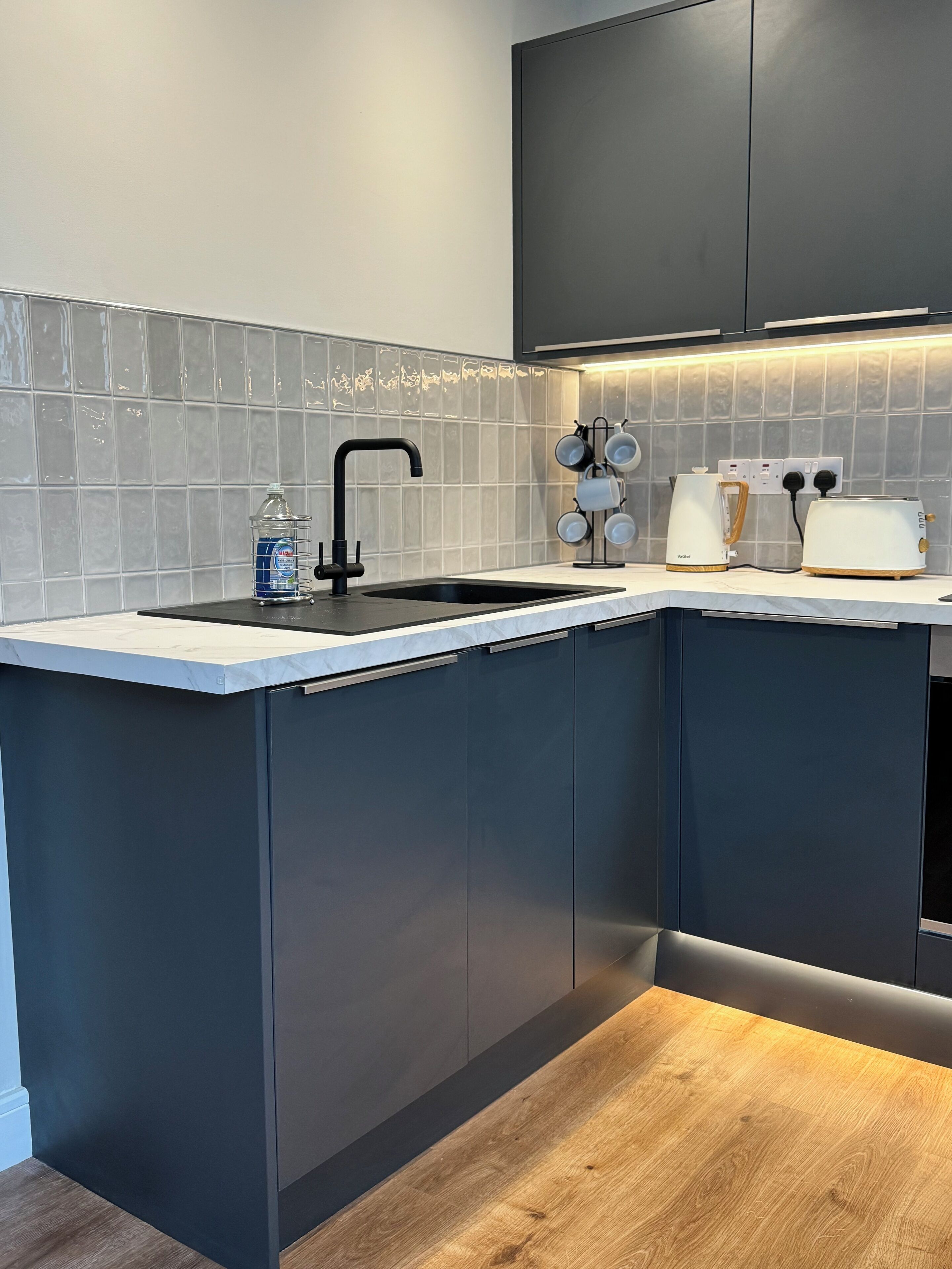 A modern kitchen with a black sink, a water dispenser, a coffee maker, and a toaster.