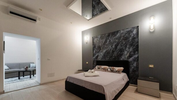Ein modernes Schlafzimmer mit Bett, Nachttischen, einer kleinen Sitzecke und Blick durch eine offene Tür.
