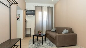 Ein Wohnzimmer mit einer Couch, einem kleinen Tisch, einem Fernseher und einem Fenster mit Vorhängen.