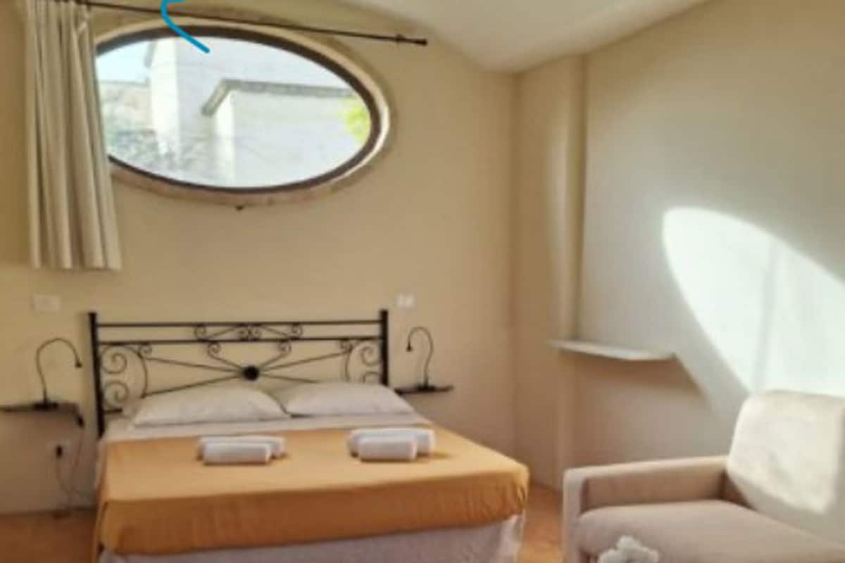 A bedroom with a bed, a round window, a sofa, and a small table.