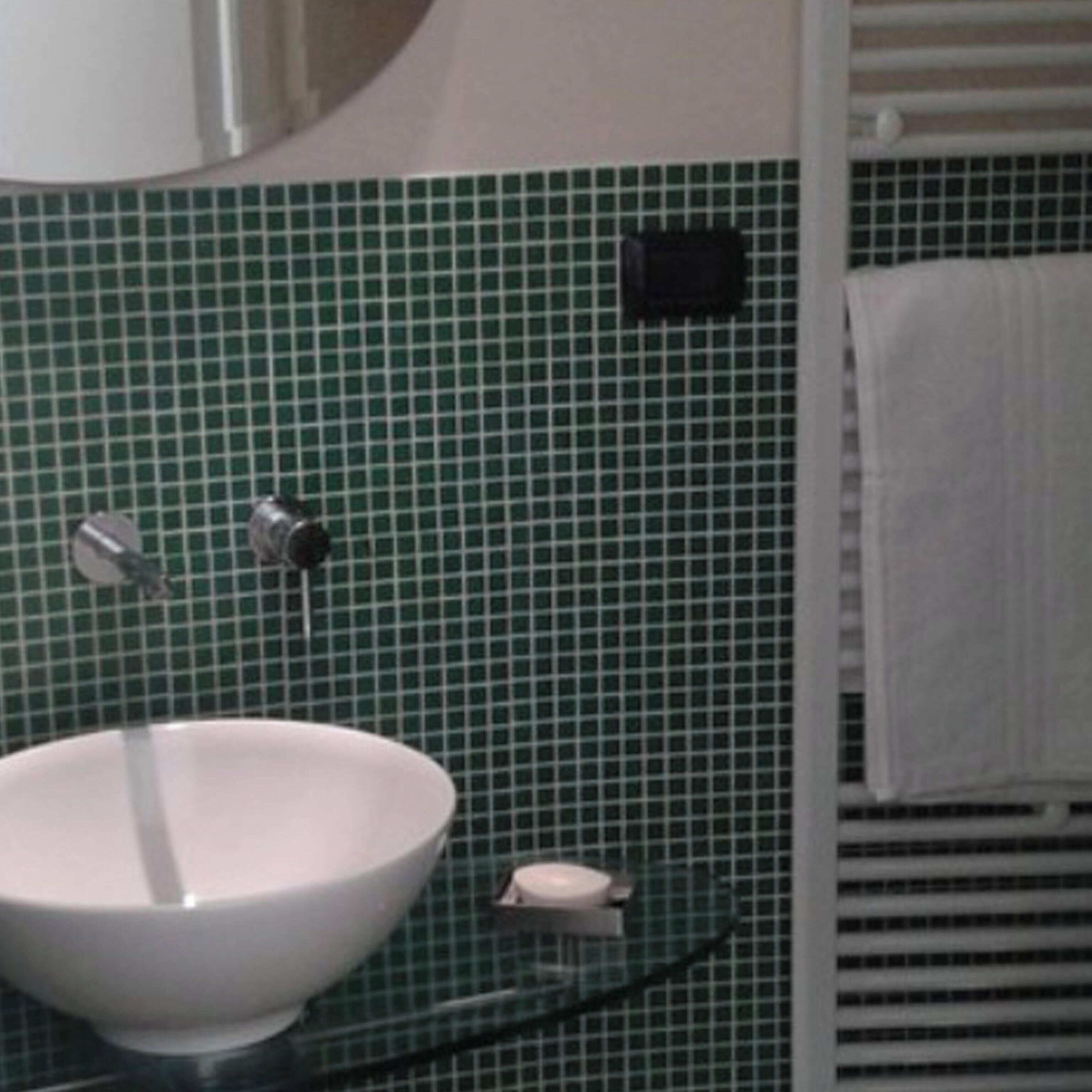 Een badkamer met een witte wastafel, groene betegelde wanden en een handdoekhouder.