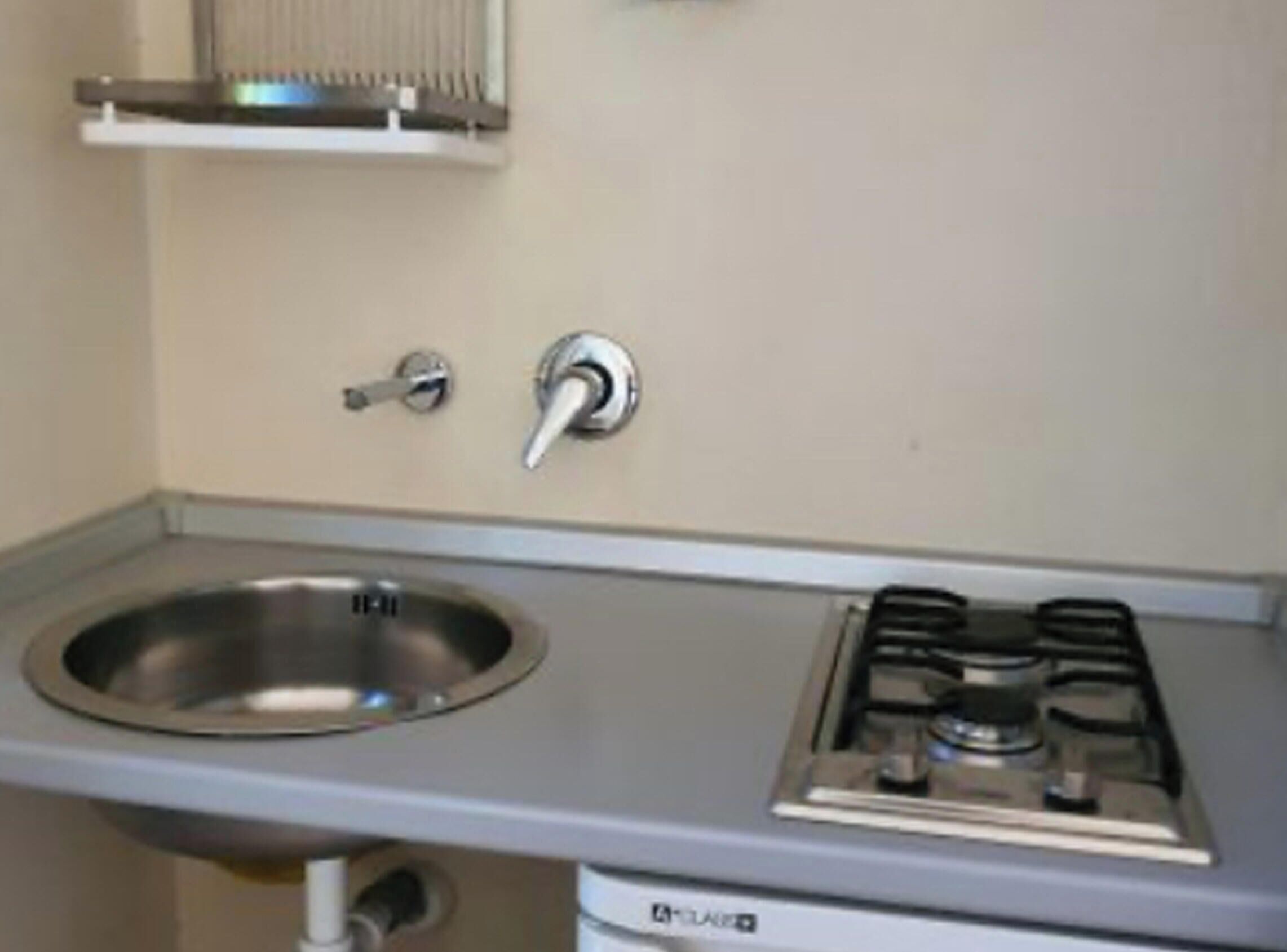 A compact kitchenette with a stainless steel sink, a gas stove, and a small shelf above the sink.