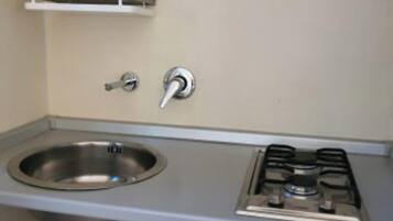 A compact kitchenette with a stainless steel sink, a gas stove, and a small shelf above the sink.