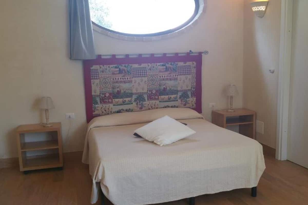 A bedroom with a bed, a headboard with a quilt, two bedside tables with lamps, and a window with a curtain.
