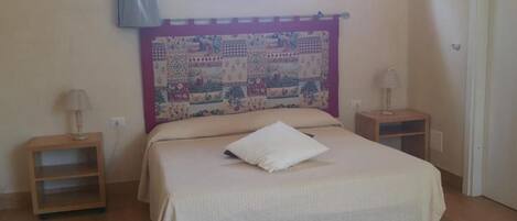 A bedroom with a bed, a headboard with a quilt, two bedside tables with lamps, and a window with a curtain.