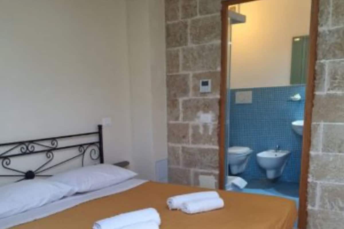 A bed with a brown bedspread, white pillows, and two rolled towels.