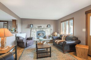 A cozy living room with leather sofas, a wooden coffee table, and a stone fireplace. - Spacious Valley View Lodge - Huge deck! (Fairplay)
