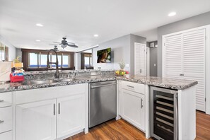 Una cocina moderna con armarios blancos, encimeras de granito, lavavajillas integrado y un refrigerador para vinos.