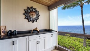 A kitchen with a wooden ceiling, a decorative sunburst wall art, and a view of the ocean. - Oceanfront - Amazing Views - Completely Renovated - Vrkcv (Kailua-Kona)