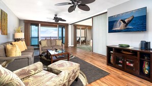 A spacious living room with a large television, ceiling fans, and a view of the ocean. - Oceanfront - Amazing Views - Completely Renovated - Vrkcv (Kailua-Kona)