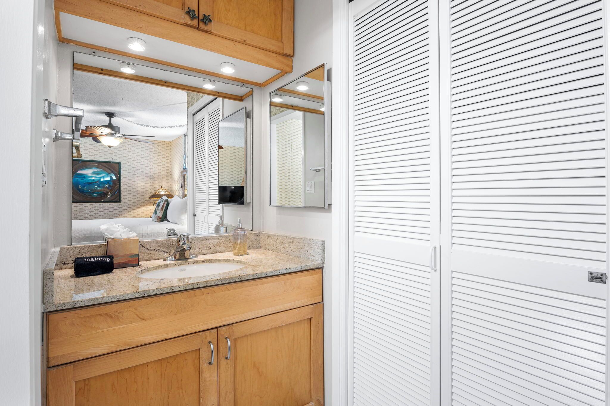 A modern bathroom with a granite countertop, a sink, and wooden cabinets. There is a mirror above the sink and a ceiling fan.