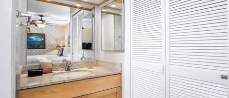 A modern bathroom with a granite countertop, a sink, and wooden cabinets. There is a mirror above the sink and a ceiling fan.