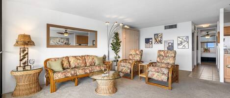 Una sala de estar con muebles de mimbre, una mesa de centro de vidrio y un espejo grande en la pared.