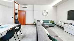 Una sala de estar moderna con un sofá, un comedor con mesa y sillas, un televisor y un reloj en la pared.
