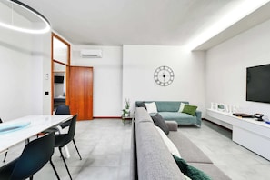 Ein modernes Wohnzimmer mit einer Couch, einem Essbereich mit Tisch und Stühlen, einem Fernseher und einer Wanduhr.