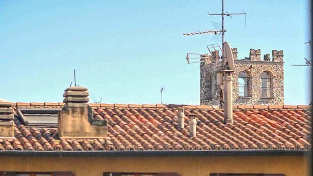 Un balcón con mesa y sillas, con vistas a un edificio con torre de piedra y tejado de tejas.