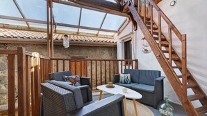 A covered outdoor seating area with wicker furniture, a table, and a wooden staircase.