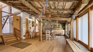 A rustic interior with wooden beams, a stone wall, and a dining area with chairs and a table.