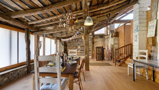 A rustic dining area with wooden beams, a chandelier, and a stone wall.