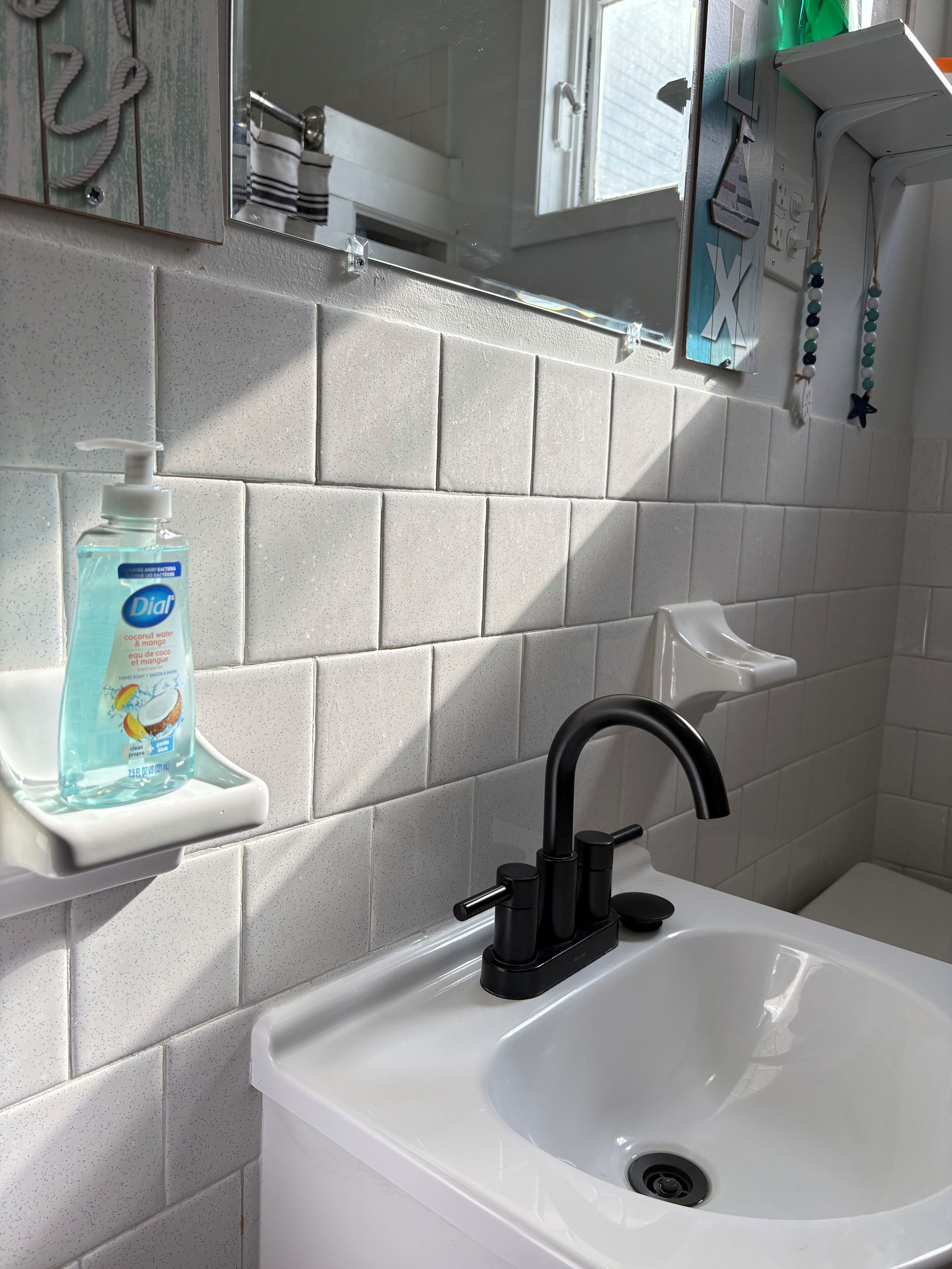 A bathroom with a white sink, a black faucet, and a soap dispenser on a white shelf.