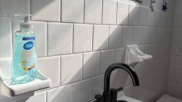 A bathroom with a white sink, a black faucet, and a soap dispenser on a white shelf.