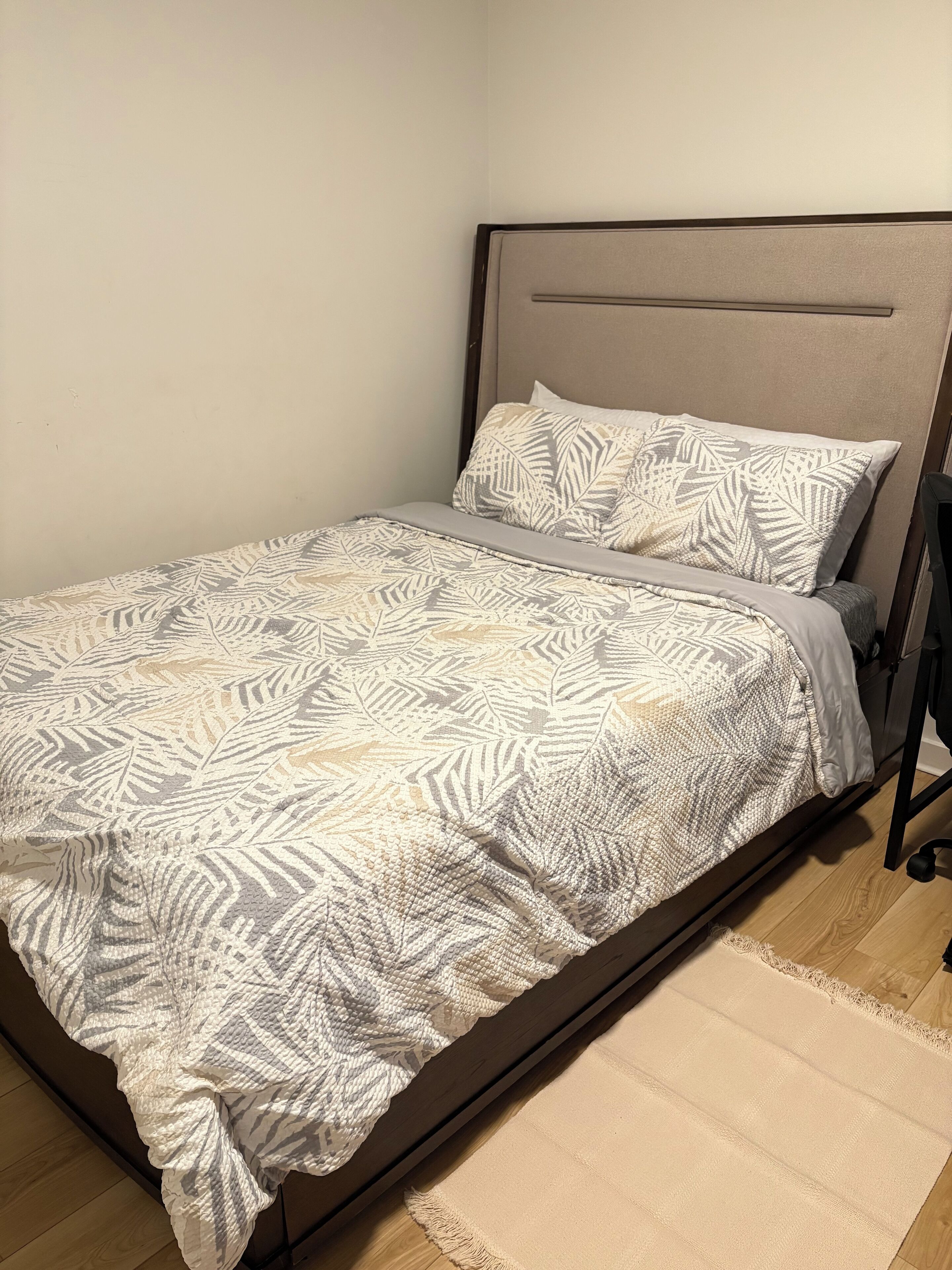 A neatly made bed with a patterned bedspread and pillows, a headboard, and a wooden floor.