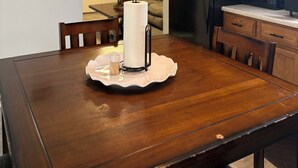 Un comedor con mesa de madera, sillas, dispensador de toallas de papel y microondas.