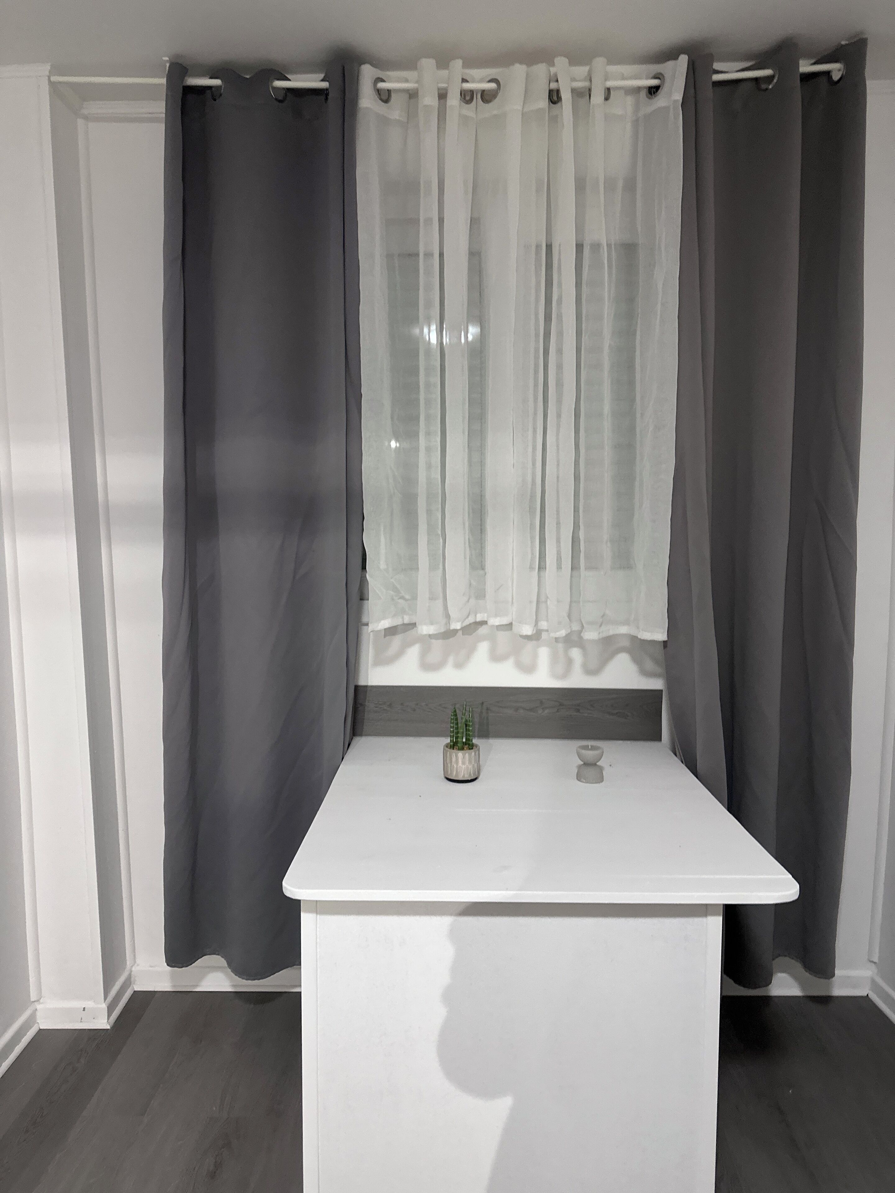 A bathroom with a white vanity, a small potted plant, and a window with sheer curtains.