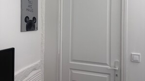 Eine weiße Tür mit schlichtem Design, ein kleiner Bilderrahmen mit einer Mickey Mouse Silhouette und dem Schriftzug "YOU ARE MAGIC" an der Wand, und eine rote Bank im Vordergrund.