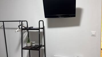 Ein Zimmer mit einem Bett, einem an der Wand befestigten Fernseher, einem Heizkörper und einem Regal mit Pflanze und Tastatur.