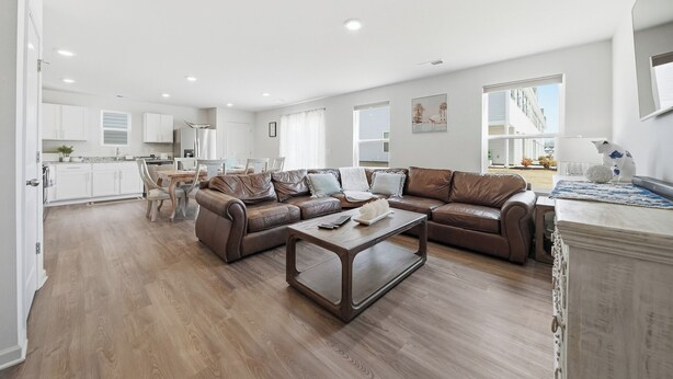 Un salon moderne avec un canapé en cuir marron, une table basse en bois et un coin repas comprenant une table et des chaises blanches.