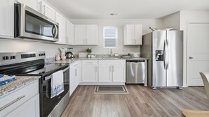 Une cuisine moderne avec des meubles blancs, des appareils en acier inoxydable et un plancher en bois.