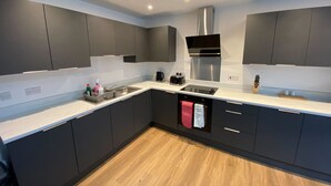 A modern kitchen with dark cabinets, a stainless steel range hood, and a white countertop. - The Square Apartments Flat 3 (Swindon)