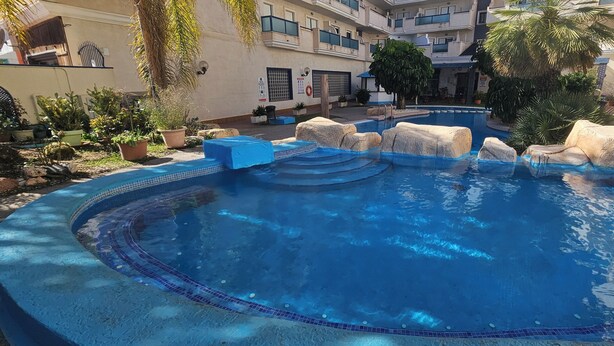 A swimming pool with a tiled edge, surrounded by rocks and potted plants. - Playa Marina, 4 min to the sea (Orihuela)