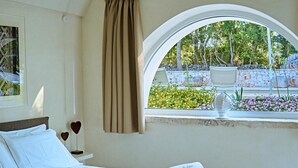 A hotel room with a bed, a window with a view of a garden, and a curtain. - Trullo Magia (Ostuni)
