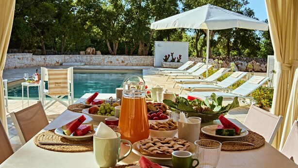 A poolside breakfast setup with a table, chairs, and a variety of food and drinks. - Trullo Magia (Ostuni)