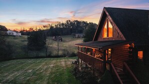 A wooden cabin with a balcony overlooking a grassy field and a sunset in the background. - Fresh Design! Creekside Cabin, Hot Tub, Dollywood! (Sevierville)