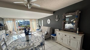 A dining area with a round table, chairs, a ceiling fan, and a view through a glass door. - Marina Giulina harbor view with jetty (Le Grau-du-Roi)