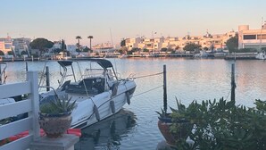 A marina with a single boat docked, calm water, and a cityscape in the background. - Marina Giulina harbor view with jetty (Le Grau-du-Roi)