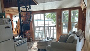 A cozy cabin interior with a kitchen, a sofa, and a staircase leading to a deck.