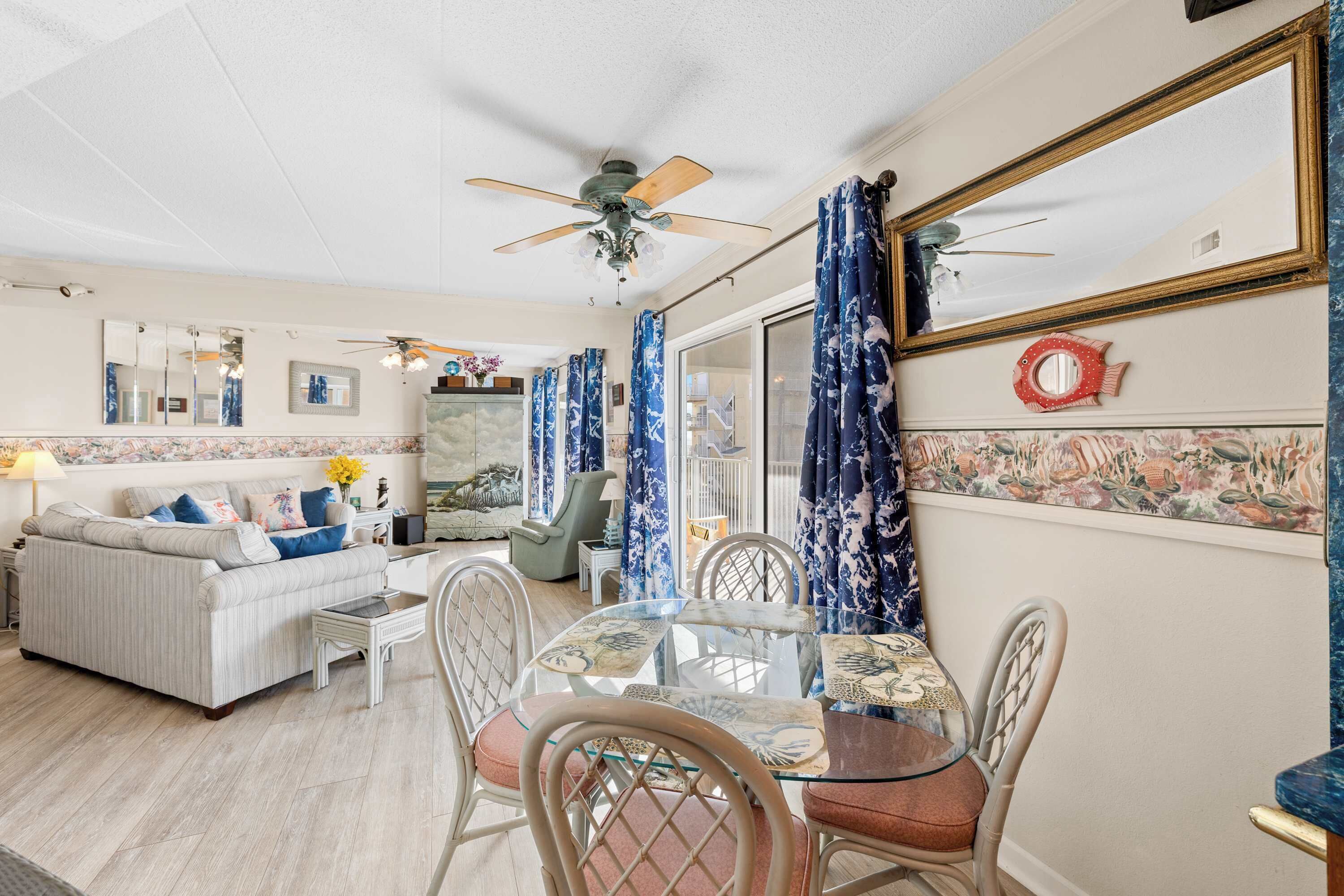 A living room with a sofa, chairs, a glass table, and a ceiling fan.