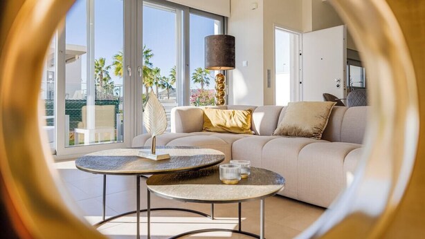 A modern living room with a sofa, two round tables, and a large window offering a view of palm trees. - Casa d'Oro neart Vistabella Golf (Orihuela)