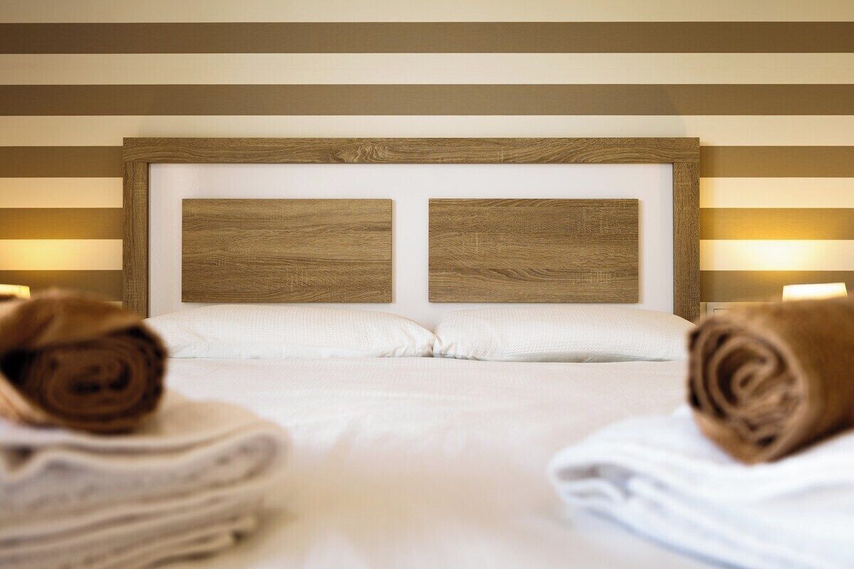 Una habitación de hotel con una cama grande, dos cabeceros de madera y dos lámparas de noche.