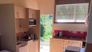 Een knus slaapkamer met een bed, een kleine kitchenette en uitzicht op een tuin.