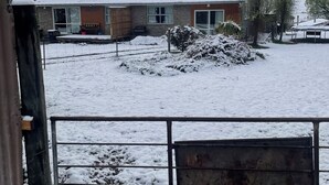 Een besneeuwd landschap met een huis met een stenen gevel, een houten terras en een omheind erf.