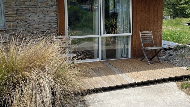 Een modern huis met een gevel van natuursteen, een houten terras en een schoorsteen.