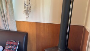 Een gezellige woonkamer met een zwarte bank, een houten wandpaneel, een zwarte kachel en een decoratieve dromenvanger.