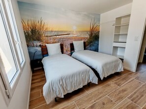 Quarto com duas camas, piso de madeira, um mural do pôr do sol e um guarda-roupa branco.