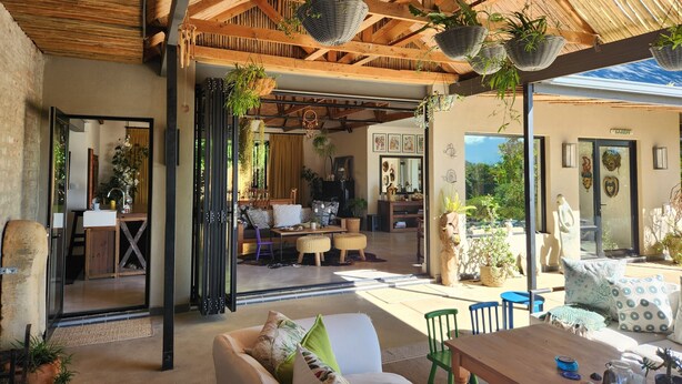 A spacious indoor area with a high ceiling and wooden beams, featuring a seating area with a sofa and chairs, a table with decorative items, and hanging planters. - Private home with exquisite mountain views in Cape Winelands (Cape Town)